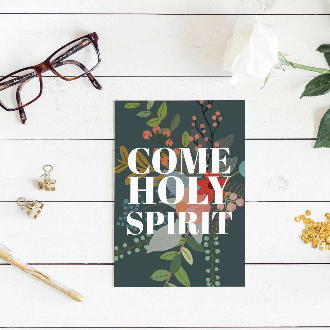 Card with 'Come Holy Spirit' text on a floral design, placed on a wooden surface with glasses and decorative items- Pink Salt Riot
