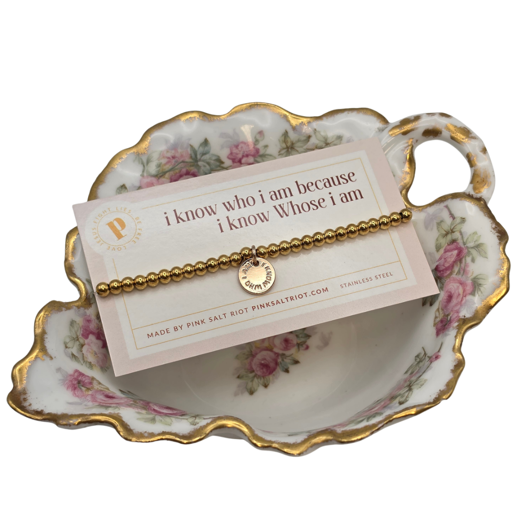Pink Salt Riot gold beaded bracelet with charm that reads "I know who I am because I know whose I am"