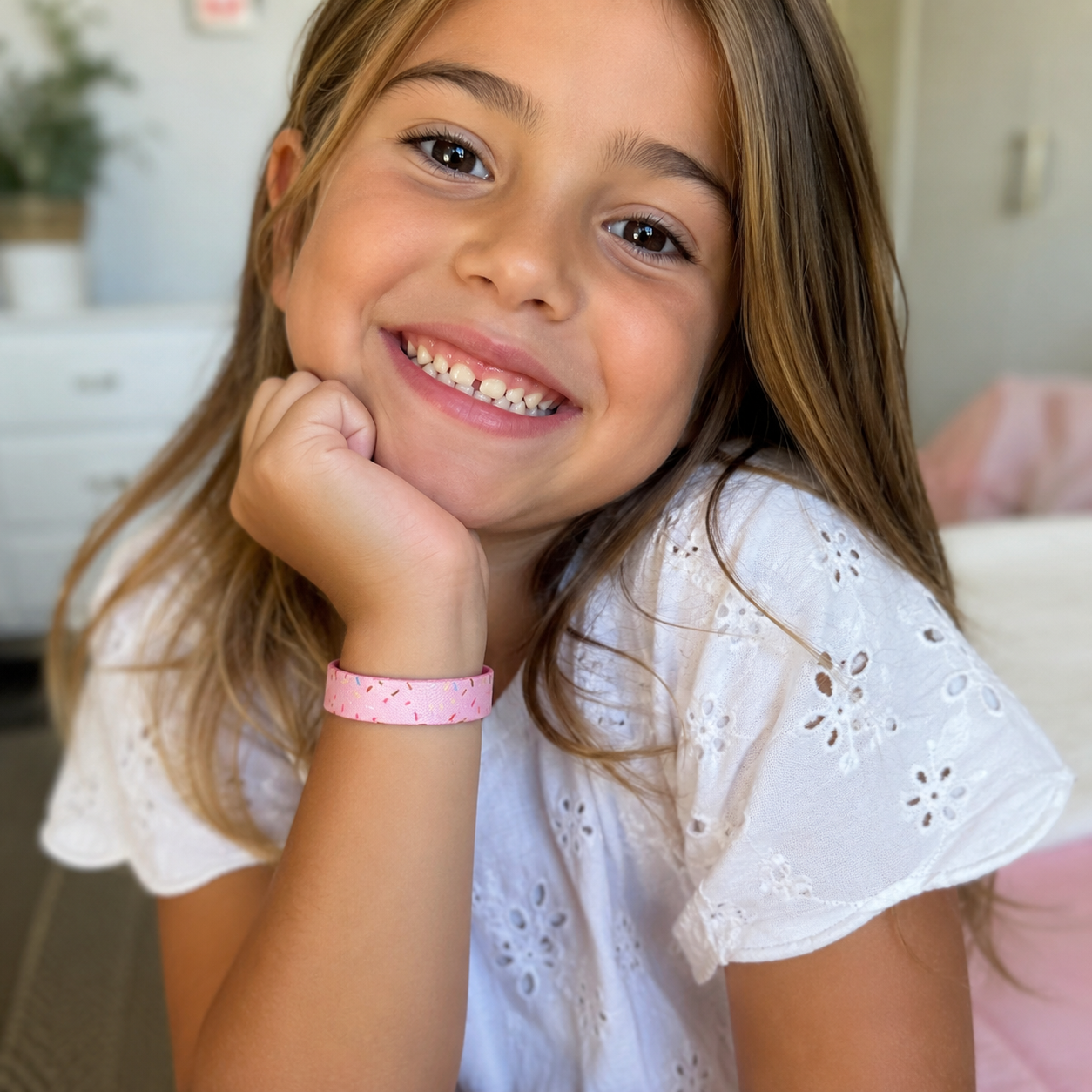 A smiling young girl wearing a light pink elastic wristband with tiny dark speckles. Pink Salt Riot- Sprinkles Kids TruthBand 